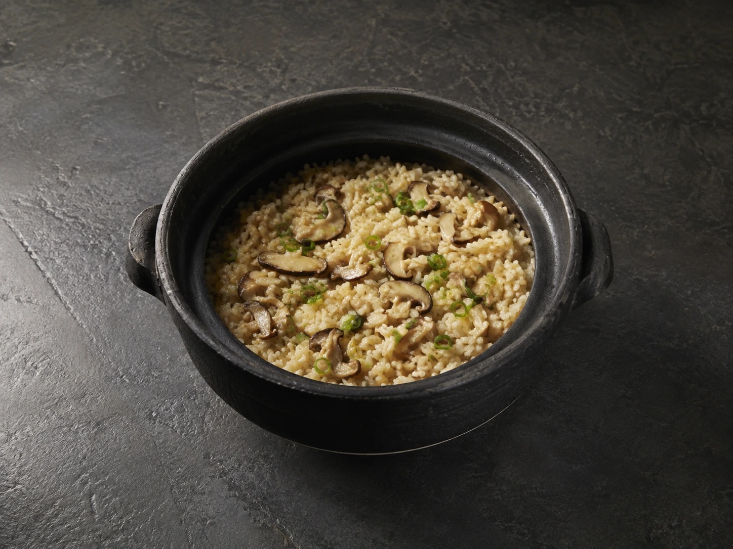 Arroz de cogumelos e cebolinha servido na panela donabe escura.